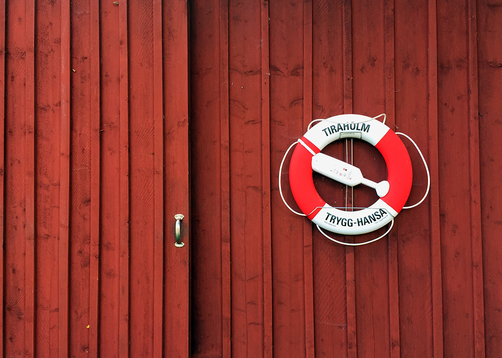 Röd-vit livräddningsboj mot röd vägg.