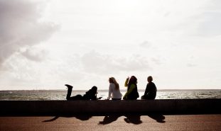Fyra sittande kvinnor på rad vid havet.