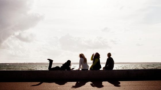 Fyra sittande kvinnor på rad vid havet.