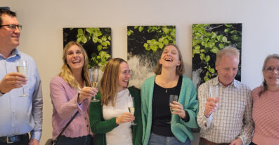 Sex personer med champagneglas i händerna ler och skrattar
